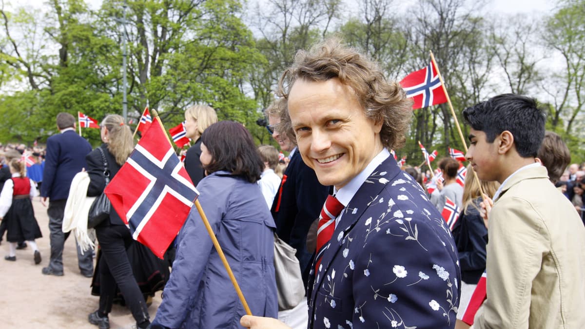 Nuori mies heiluttaa iloisesti Norjan lippua kulkueessa Norjan kansallispäivänä.