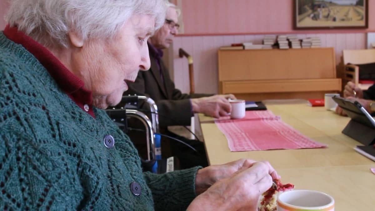Vanha nainen syö piirakkaa pöydän ääressä