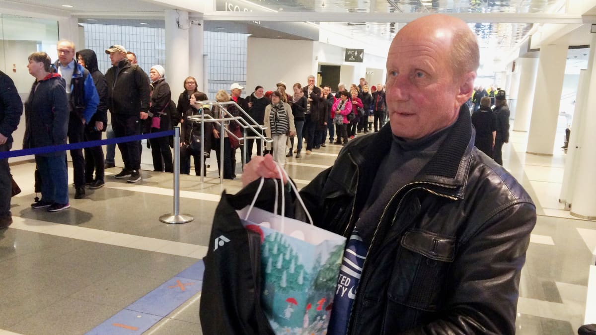 Mies pitää kädessään muumimukikassia Tampere-talon aulassa, taustalla kymmenien ihmisten jono