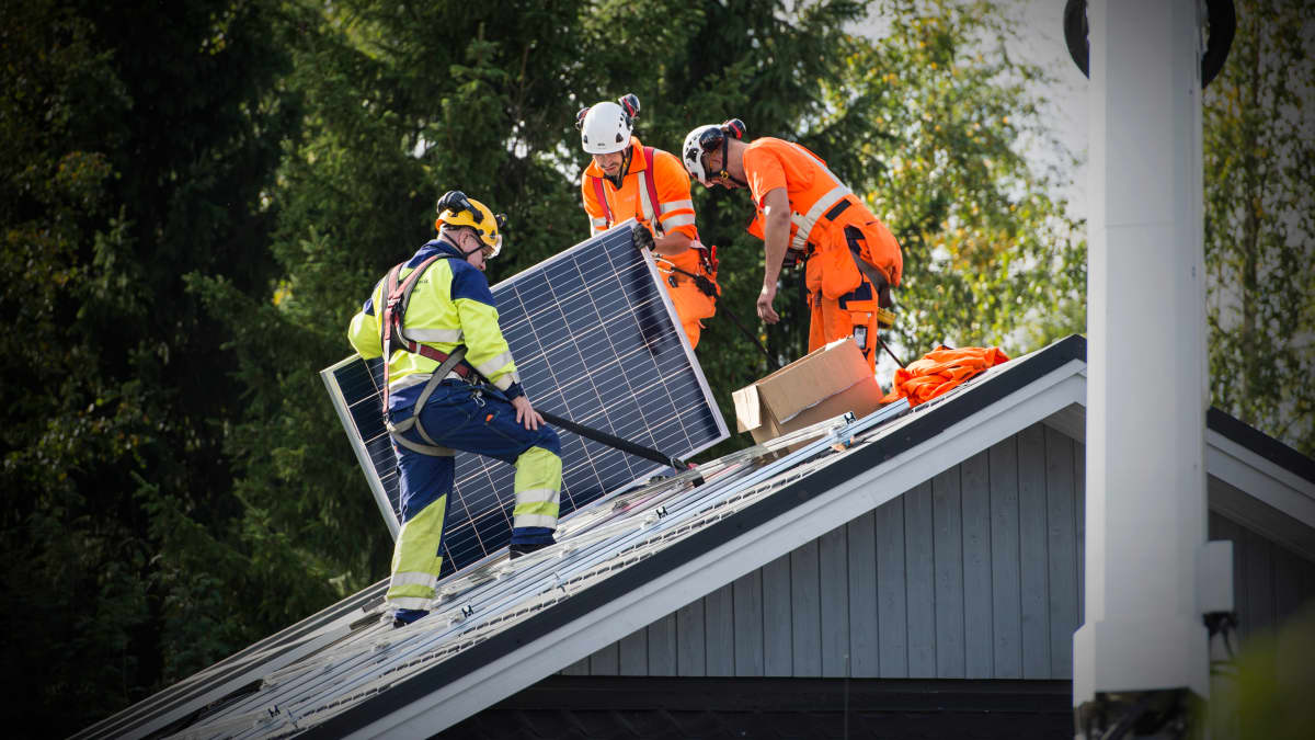 Miehiä asentamassa aurinkopaneeleja katolle.