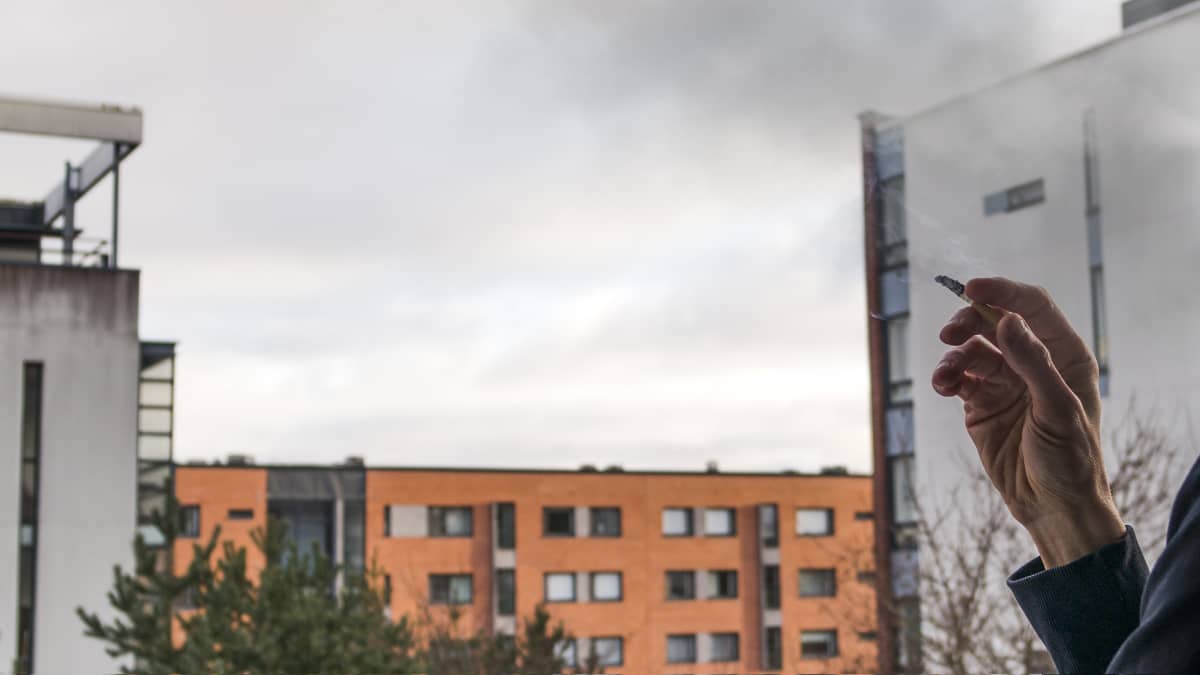 Miehen käsi pitelee palavaa tupakkaa parvekkeella.