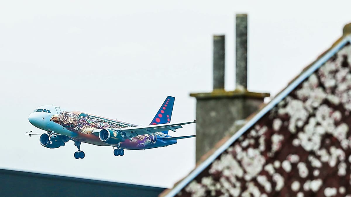 Brussels Airlinesin kone lähestyy Brysselin lentoasemaa, etualalla rakennuksen kattoa ja savupiippu.