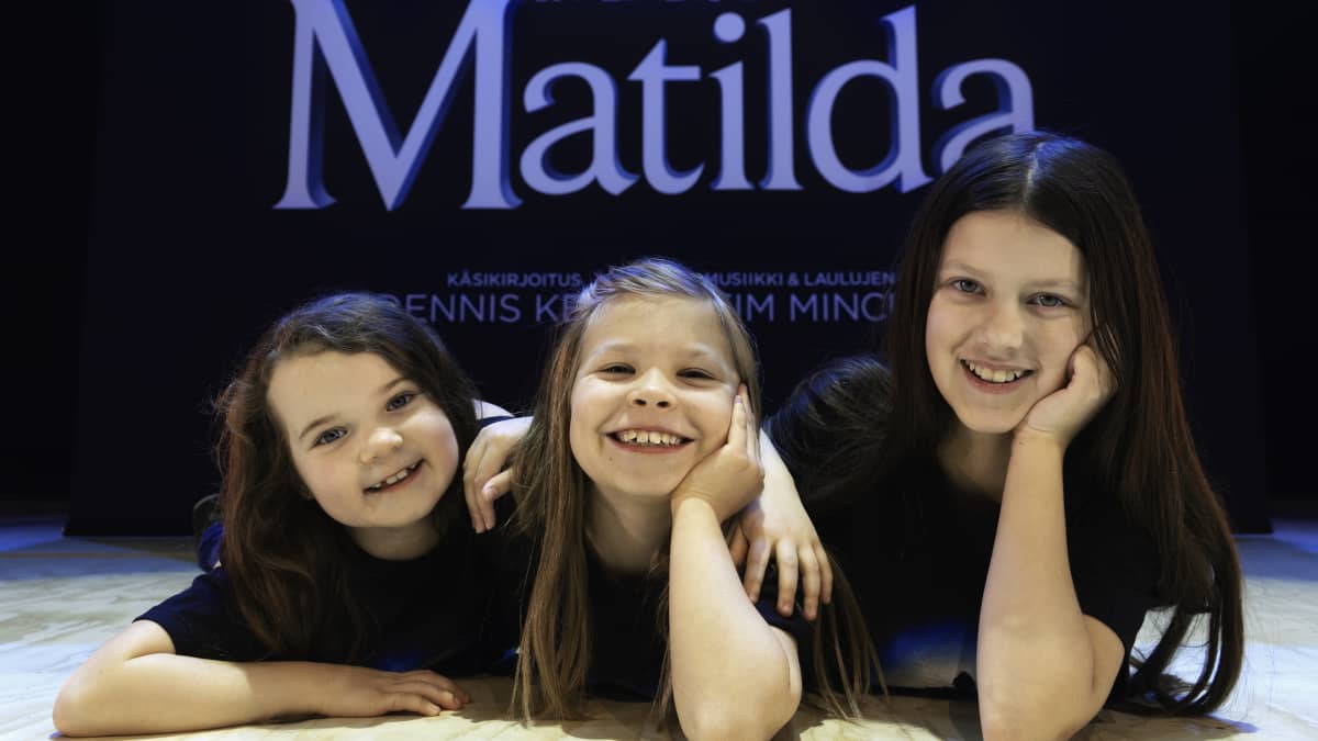 Kolme tyttöä makaa maassa Matilda-kyltin edessä.