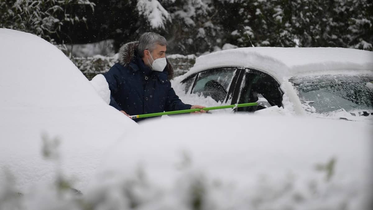 Kuvassa harmaahiuksinen mies puhdistaa auton ikkunoita lumesta. 
