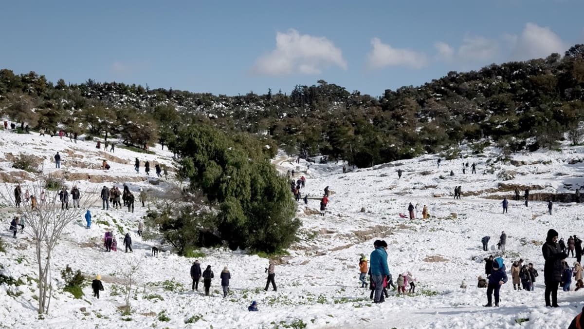 Kuvassa on ihmisiä kävelemässä lumisessa rinteessä. 