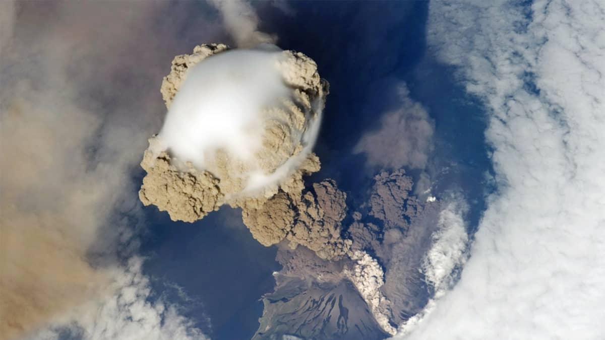 Ylhäältä otettu kuva ruskeasta pilvestä, joka nousee tulivuoresta maapallon pilviverhon läpi. 