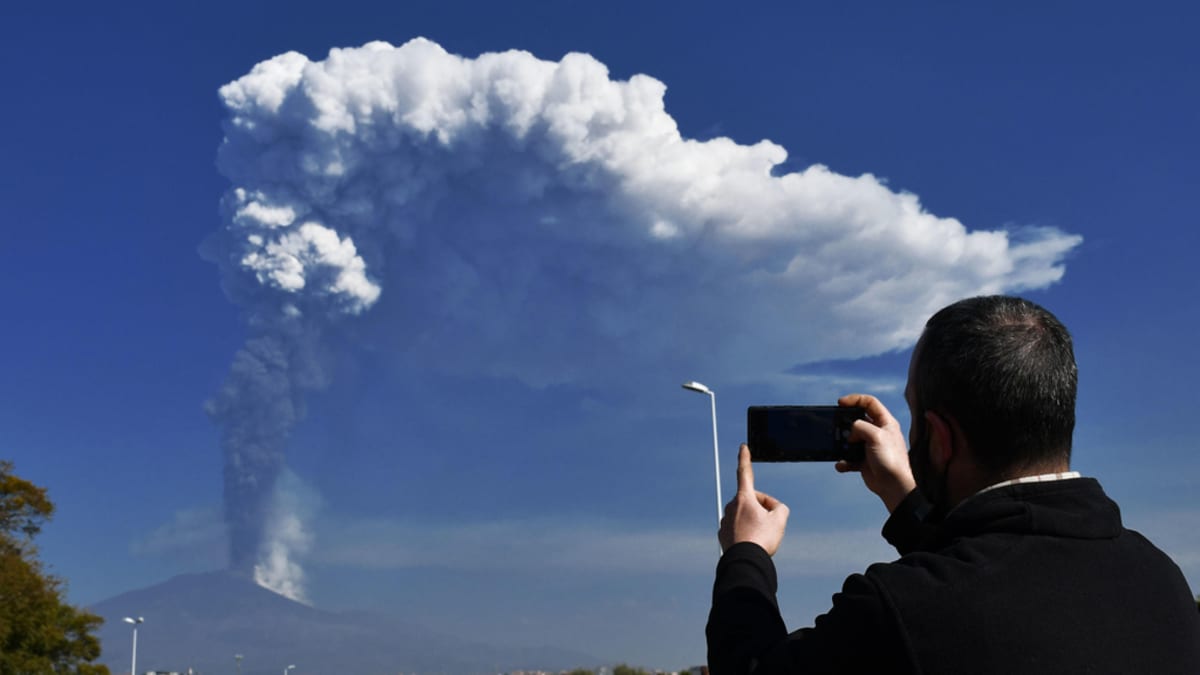 Mies ottaa kännykkällään kuvaa  etäisyydessä savuavasta Etnasta. 