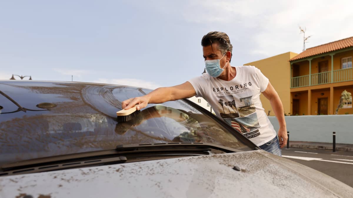 Mies puhdistaa tulivuoren tuhkaa autonsa tuulilasista. 