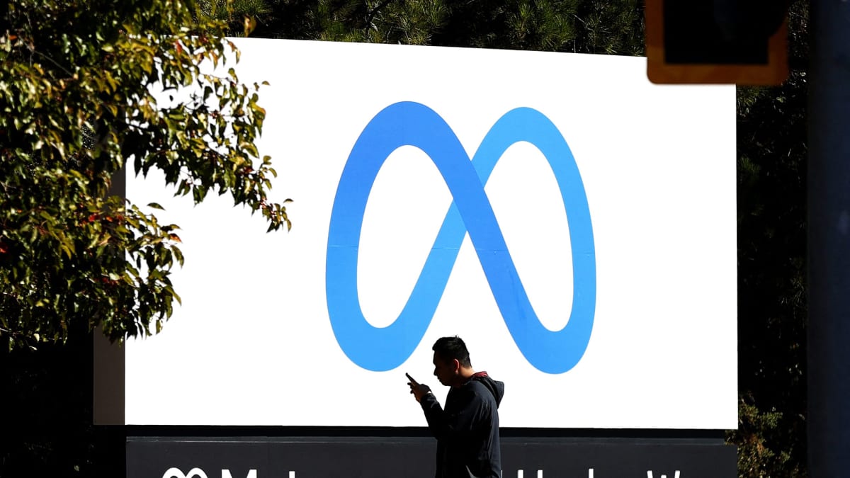 Kännykkää tuijottava mies kävelee Meta-yhtiön logon editse yhtiön pääkonttorin edustalla Menlo Parkissa.