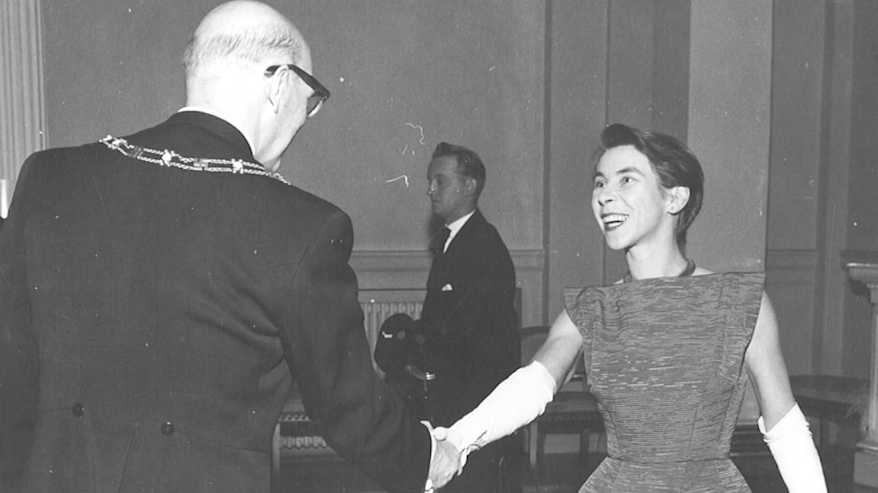 Mustavalkoisessa vanhassa valokuvassa juhlatilanteessa iltapukuun pukeutunut henkilö kättelee selin olevaa pukuun pukeutunutta henkilöä, tasavallan presidentin itsenäisyyspäivän vastaanotto.