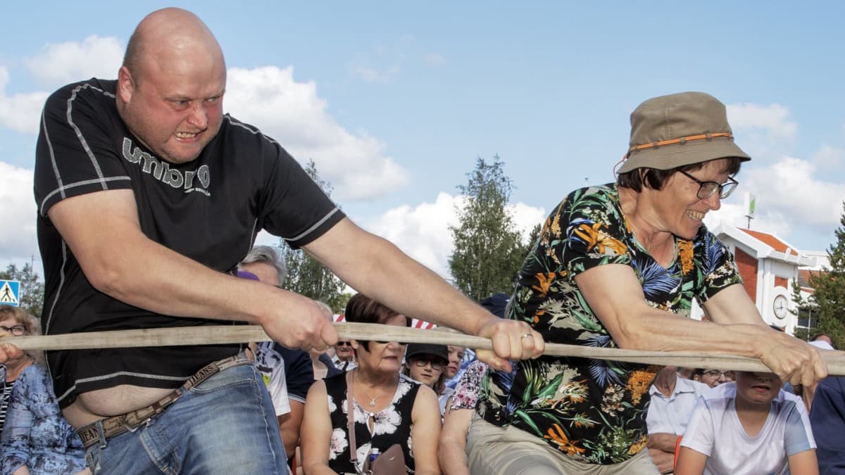 Nainen ja mies vetävät köyttä samalla puolella. Kovat irvistykset.