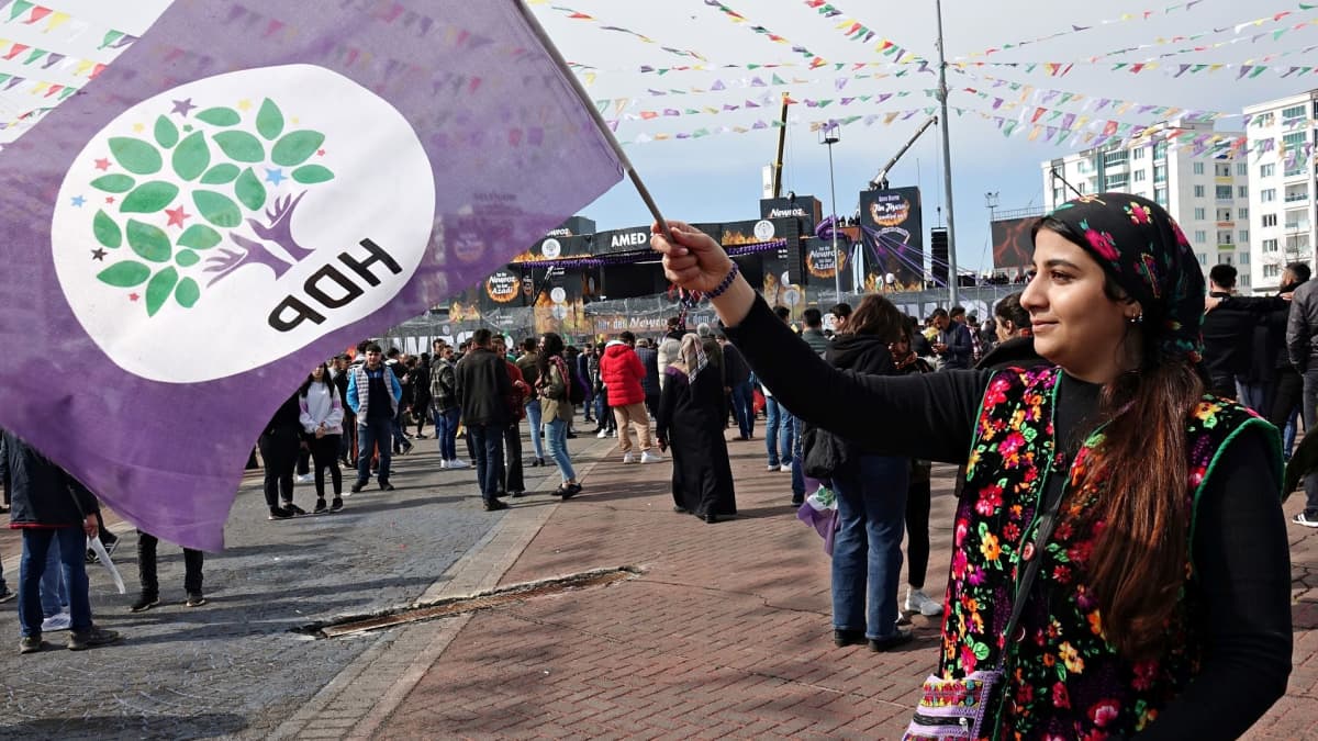 Nainen pitelee kurdipuolue HDP:n lippua. Taustalla on väkijoukko.