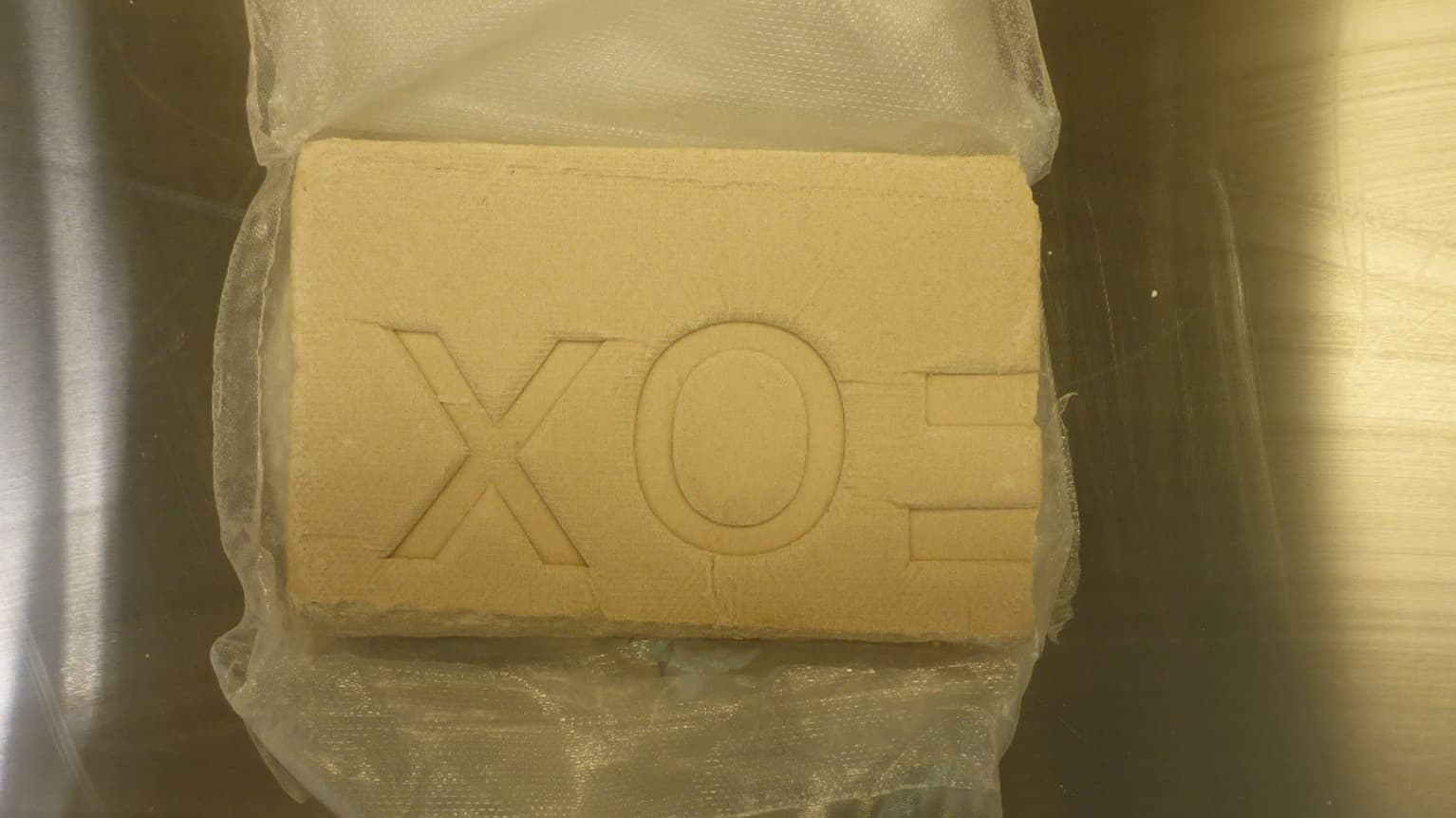 Läpinäkyvä muovipussi, jossa kellertävä kuutiomainen möykky huumausainetta, möykyn päällä erottuu teksti FOX.