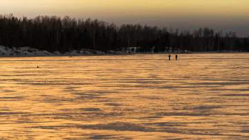 Retkiluistelijat järven jäällä. Iltaruskoa. 