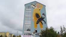 Koulurakennuksen päädyssä oleva suuri seinämaalaus, jossa seisoo kelta-asuinen lapsi. Mukana myös eläinhahmoja.