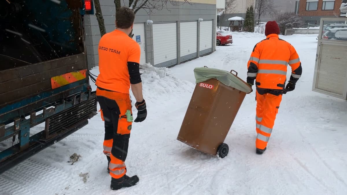 Kaksi roskakuskia työssään kiinteistön jätekatoksessa. Toinen vie paikalleen biojäte-astiaa.