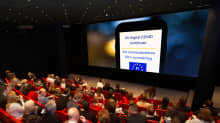 Elokuvateatterin yleisö katsoo valkokankaalla olevaa koronapassia.