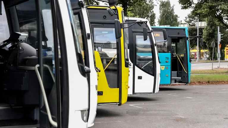 Fyra bussar i olika färger står uppradade på en busstation i Tavastehus. 