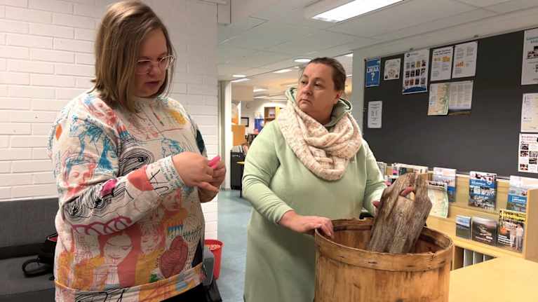 Vapaa-aikasihteeri Kaisa Tapiola-Länsman ja kunnanjohtaja Päivi Kontio tutustuvat kala- tai marjan sälytykseen tarkoitettuun astiaan.