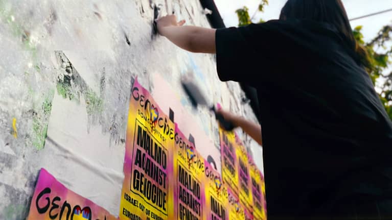 Kvinna som hänger upp färgranna planscher med texten Malmö against genocide.