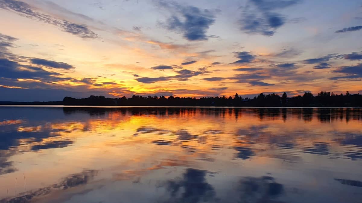 Illan viimeiset auringonsäteet. Iltaruskoa tyynen järven yllä, pilviä kasaantuu taivaalle. 