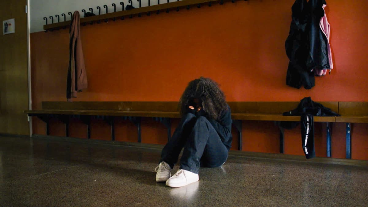 Ensam flicka sitter i skolans korridor. 
