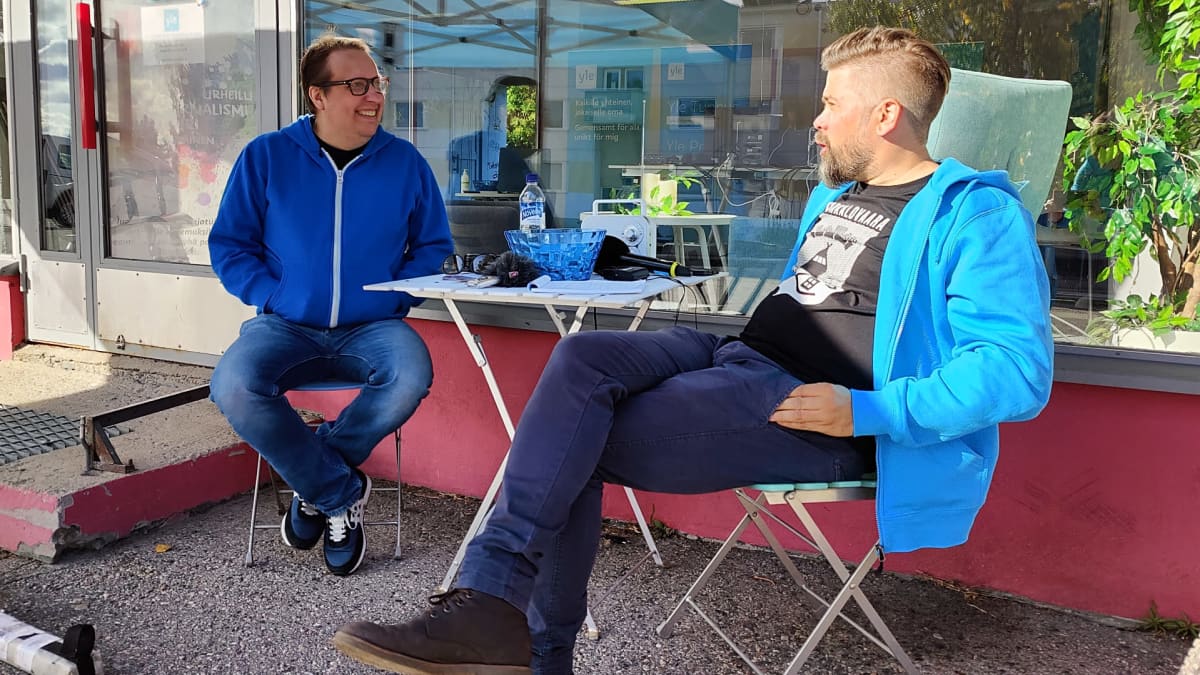 Marko Niemelä (vas.) ja toimittaja Ari Hursti istuvat penkeillä rakennuksen edessä.