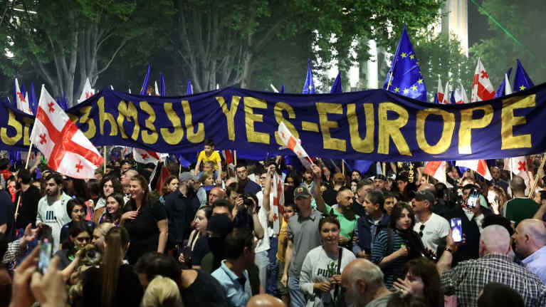 Mielenosoittajia kulkee Tbilisin kaduilla ison sinisen banderollin kanssa, jossa lukee "Kyllä Eurooppa".