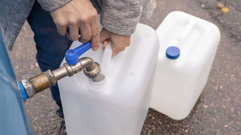 Ihminen pitelee vesikanisteria ja laskee vettä isommasta säiliöstä kanisteriin.