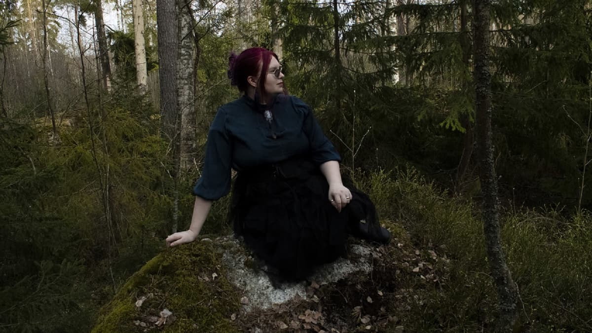Kirjailija Serafia Alho istuu kiven päällä metsässä. 