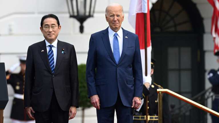 Japanin pääministeri Fumio Kishida ja Yhdysvaltain presidentti Joe Biden seisovat Valkoisen talon pihassa. Taustalla sotilaat pitelevat maiden lippuja.