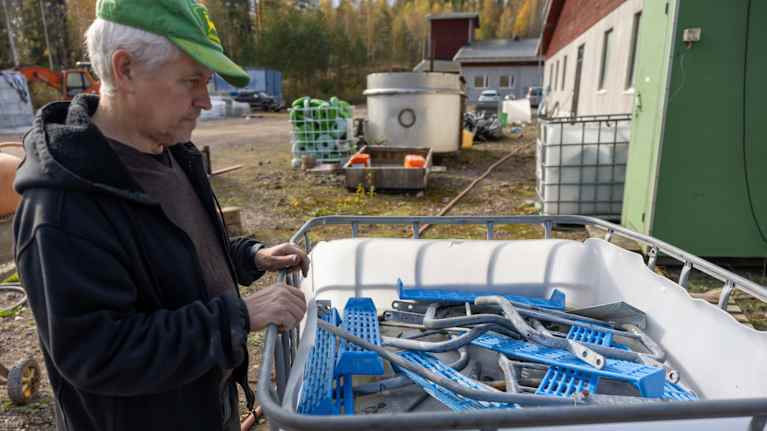 En medelålders man, Guy Bosas, står vid en stor vit plastbunke som innehåller tvållösning och metalldelar.
