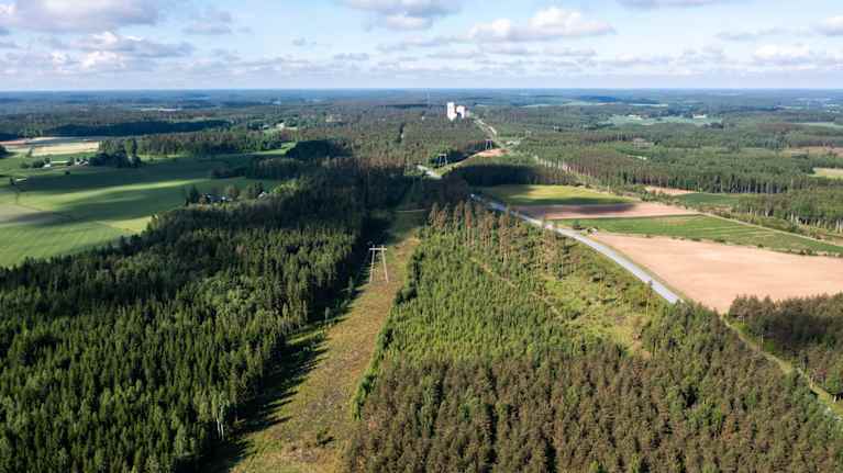 Flygfoto över ett vidsträckt skogsområde med några öppna fält och en stor ellinje under en delvis molnig himmel. Ingen synlig text i bilden.