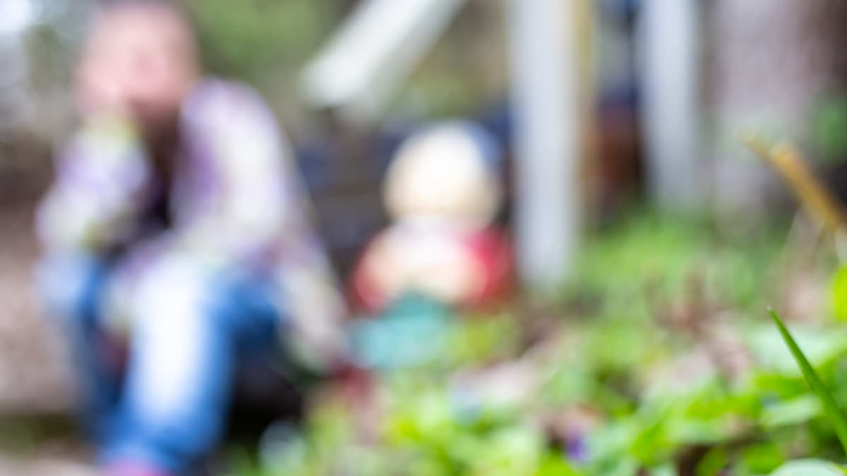 Etualalla sinikukkaisia kasveja, taustalla epäskarppina aikuinen ja lapsi.