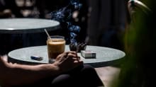 Anonyymi ihminen juo kahvia ja polttaa tupakkaa aurinkoisella terassilla. 