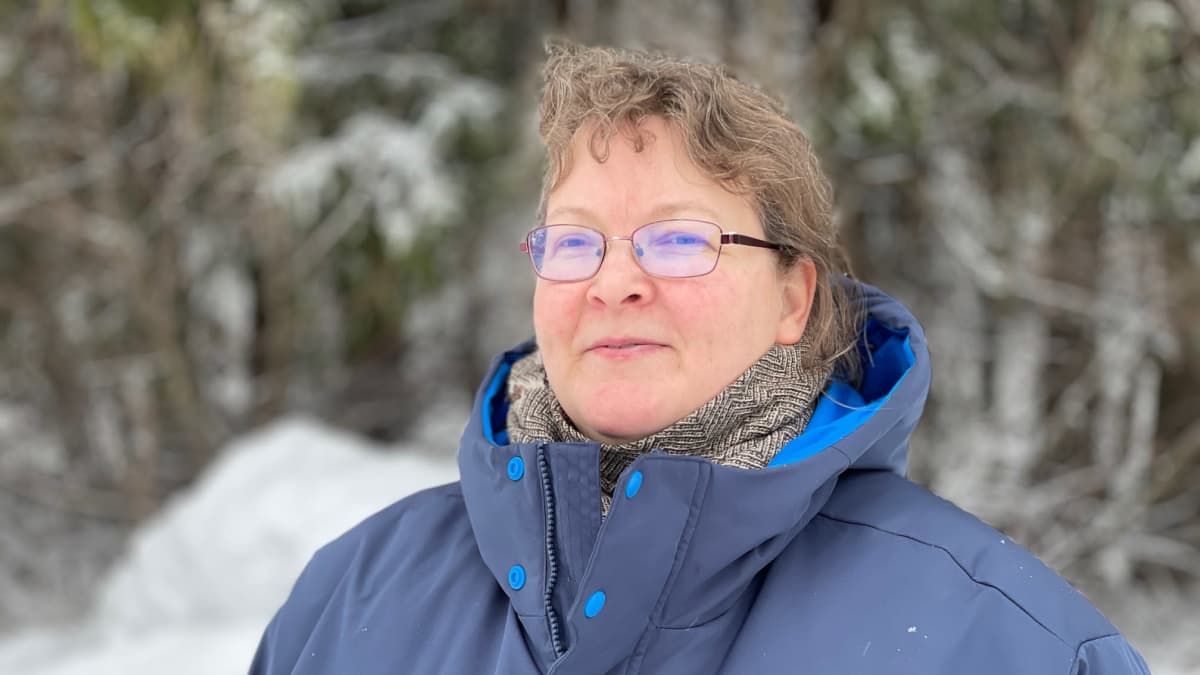 Koirakouluttaja Susanna Hämäläinen seisoo lähikuvassa talvisessa maisemassa retsän reunalla.