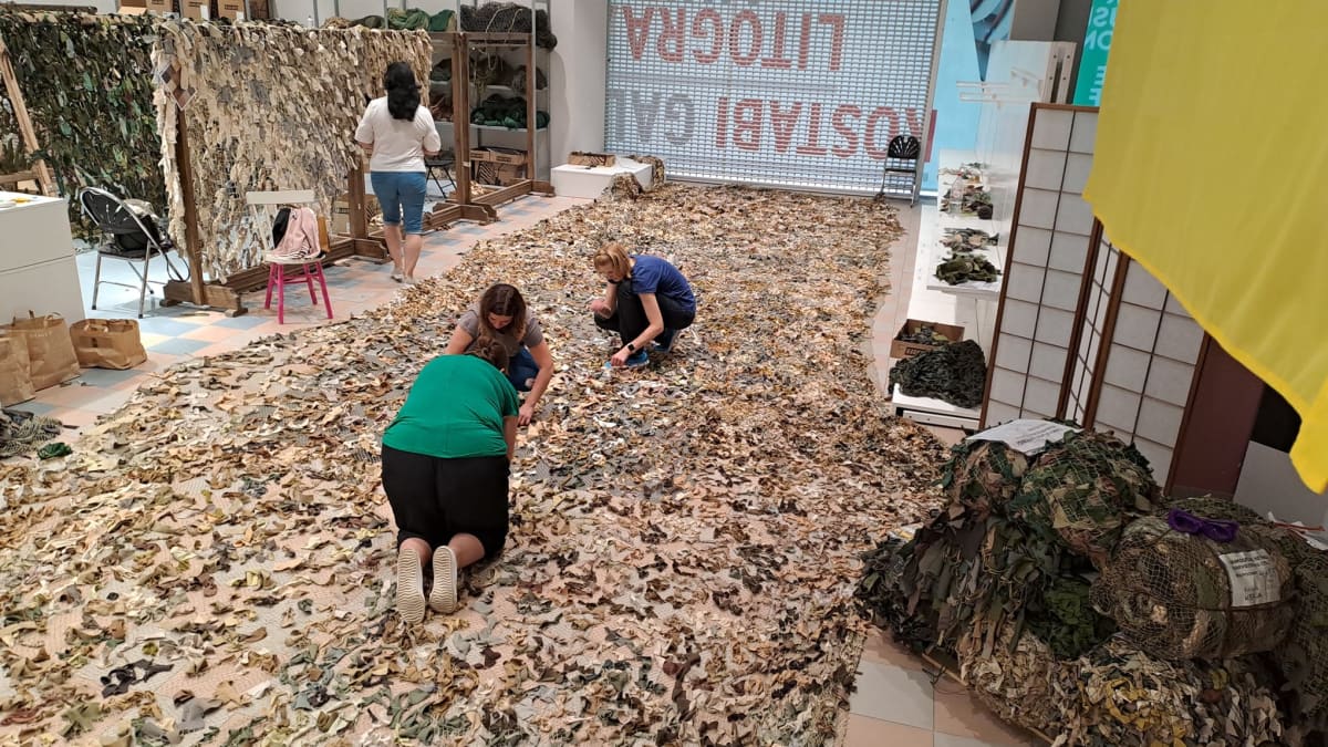 Virolaisia tekemässä käsityönä naamioverkkoa Ukrainaan lähetettäväksi. Naamioverkkoa tehdään pienistä käytetyistä tekstiilinpalasista lattialla.