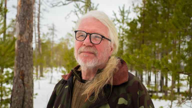 Vaalea pitkätukkainen biologi Vesa Hyyryläinen maastopuvussaan kainuulaisella talvisella suolla.