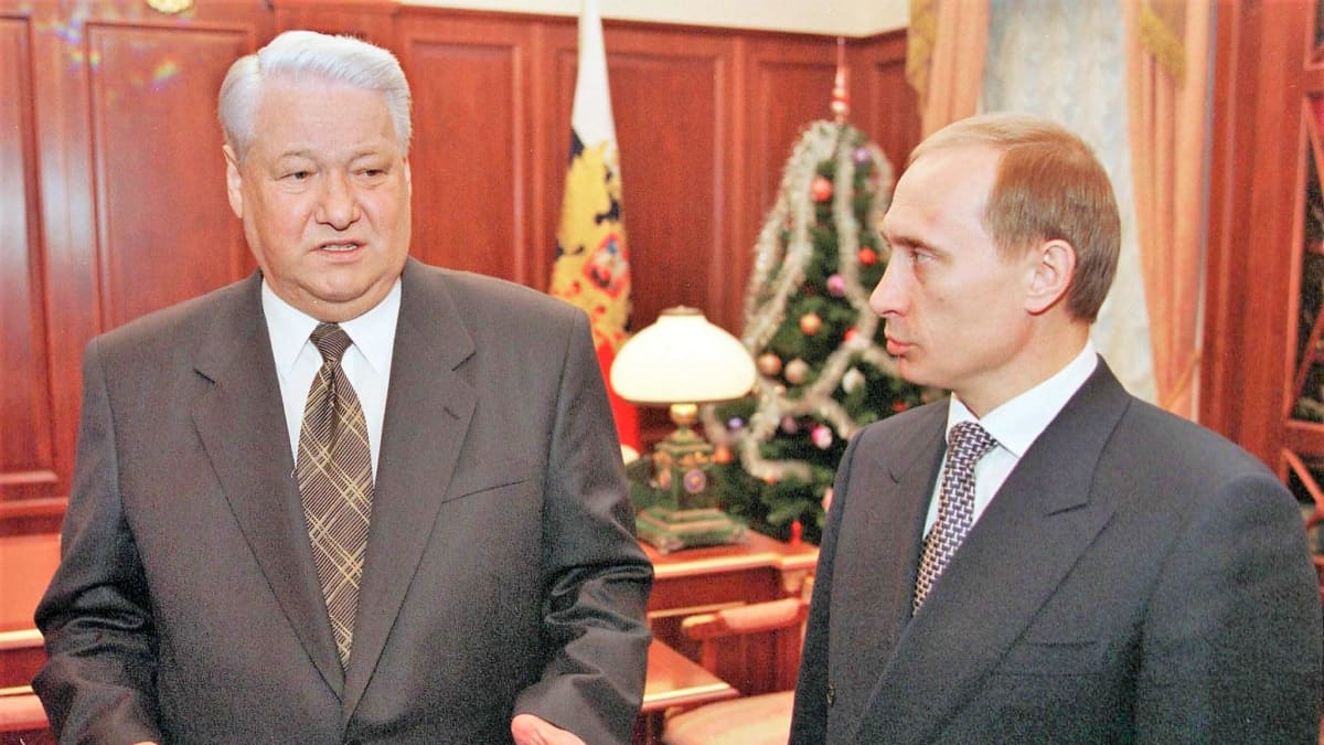 Jeltsin puhuu ja Putin kuuntelee. Miehillä on tummanharmaat puvut. Jeltsinin kravatissa on ruutukuviota, Putinin kravatissa pilkkukuviointi. Taustalla kabinetissa näkyy joulukuusi ja Venäjän lippu.