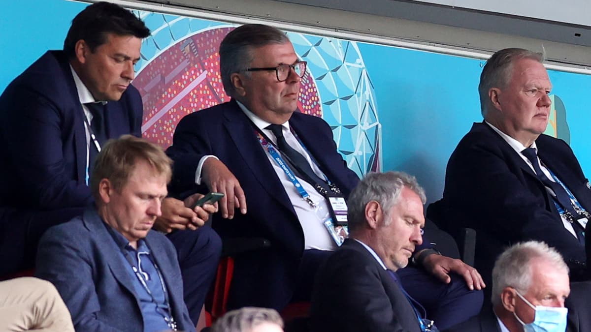 Ari Lahti sitter iklädd kostym på en läktare omgiven av andra åskådare.