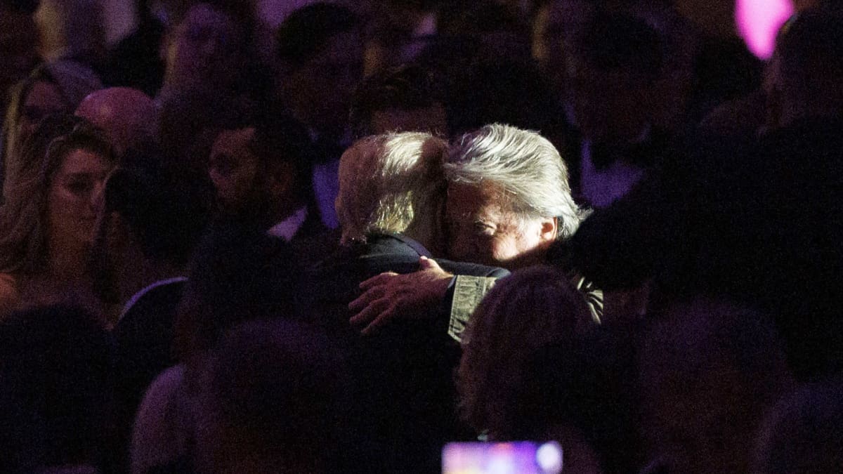Trump ja Steve Bannon halaava, aika tumma kuva, jossa korostuvat miesten vaaleat tukat. 
