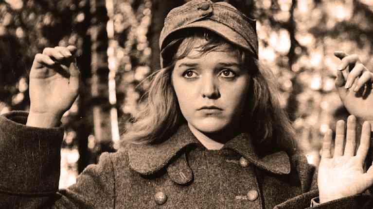 Elina Salo i Lottauniform med uppsträckta händer i en skog i femtiotalsfilm.