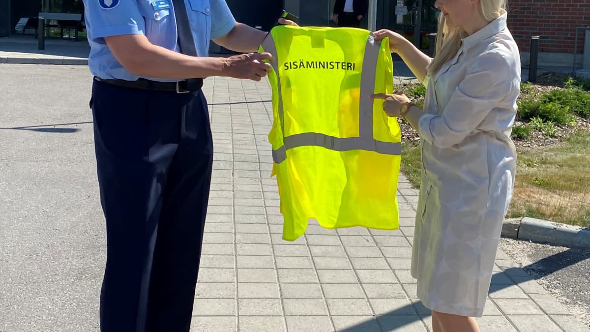 Sisäministeri Maria Ohisalo pitelemässä poliisin avulla turvaliiviä, jossa lukee sisäministeri.