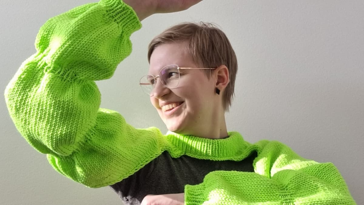 Käsityöharrastaja Sanna Pyykönen on pukeutunut neulomaansa kirkaanvihreään boleroon, joka muistuttaa Käärijän hihoja.