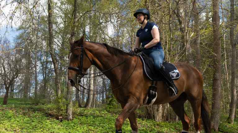 Jonna Aaltonen ruskean hevosen selässä keväisessä säässä.