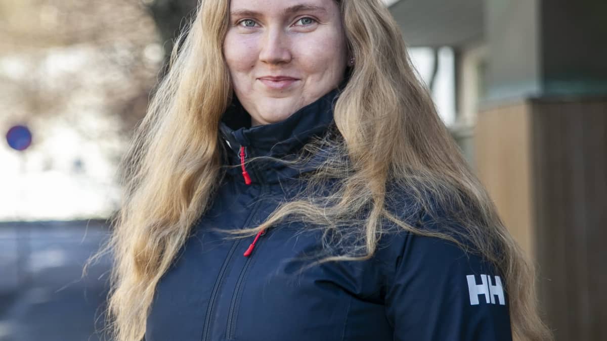 Venla Kärkkäinen katsoo suoraan kameraan kerrostalon pihalla. 