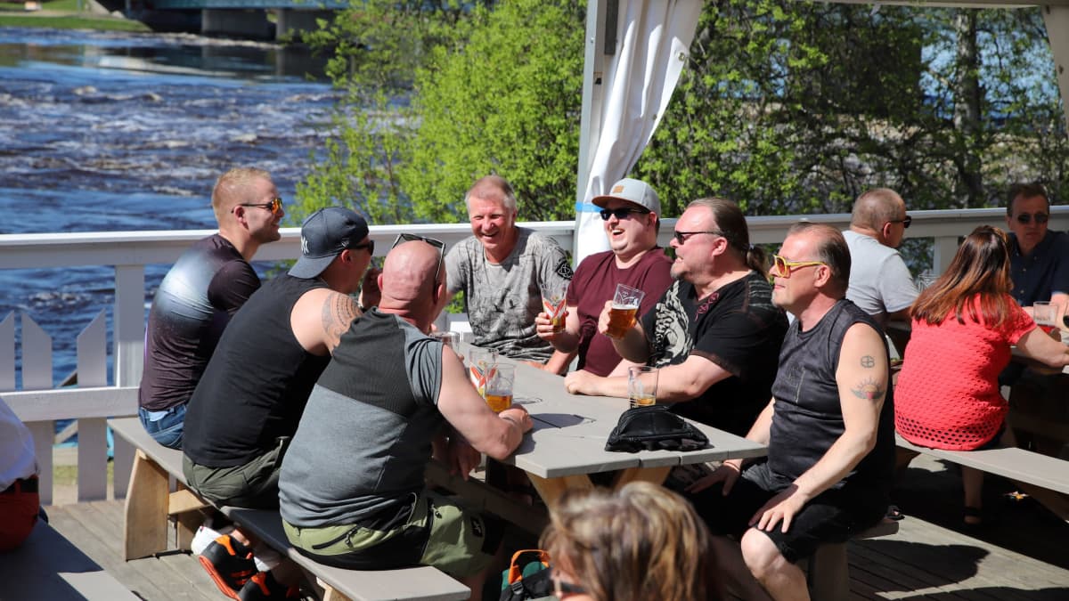 Miehiä istumassa terassipöydässä Rovaniemellä, taustalla tulviva Kemijoki.