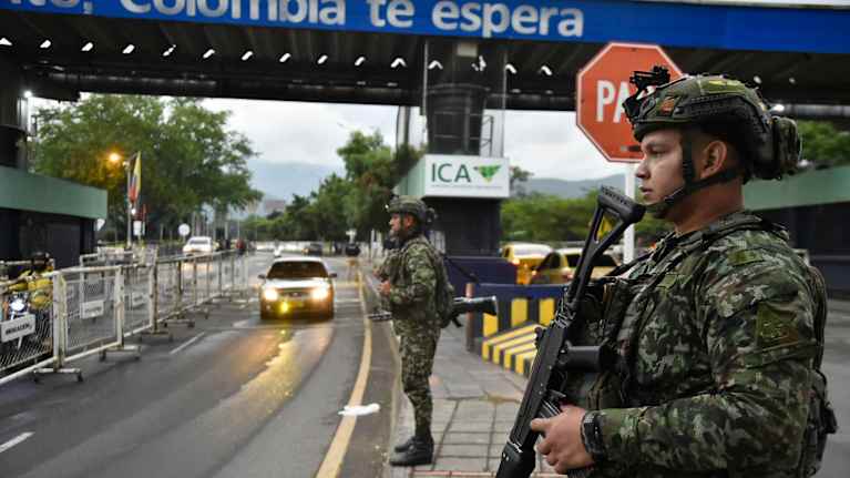 Tungt beväpnde soldaer står på en gata  nedanför en bro.