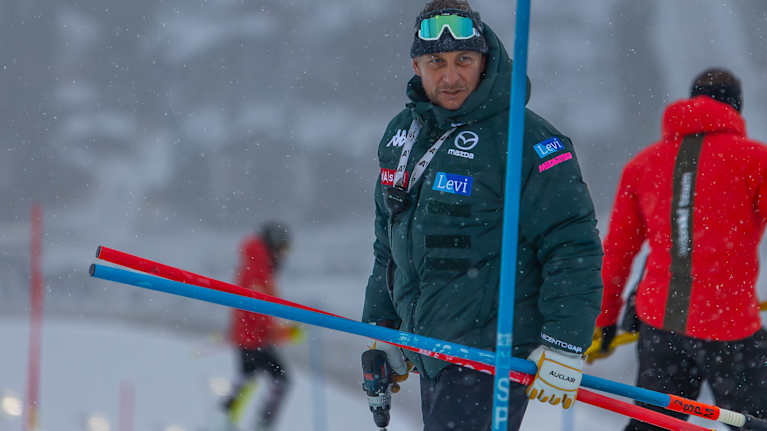 Suomen miesten alppimaajoukkueen päävalmentaja Mario Rafetzeder seisoo rinteessä pujottelukepit kädessään.