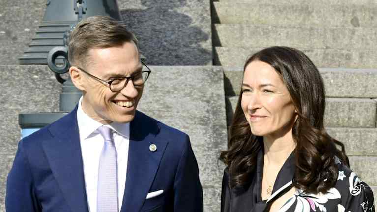 A smiling man and woman in dark formal attire stood outdoors in the sun.